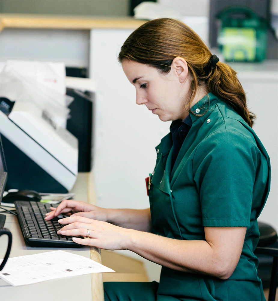A nurse working at a computer station in a clinical setting, used to review nursing workplaces and view nursing employer ratings.
